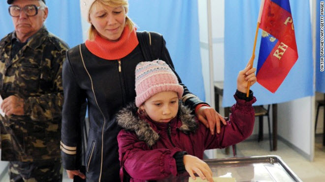 طفلة تلقي بورقة إقتراع والدتها وهى ترفع العلم الروسي في مركز للاقتراع يوم الأحد 16 مارس